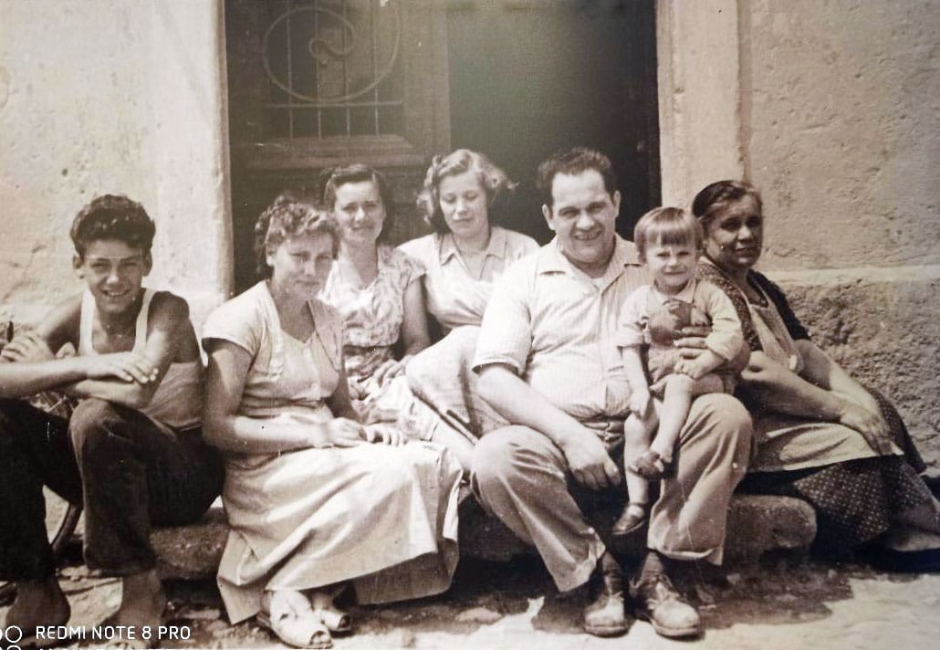 11 - Slika pred gostilno Vitorje. Družina Vitorje Frandolič pred vhodom današnje gostilne »Pri Andreju«. Od leve: Drejče, Elda, Nada, Marija, moj oče Aldo z mano v naročju in njegova sestra Vitorja por. Ferfoglia. Koje teta Vitorja kupila teve aparat,sem začel zahajati k njej na ogled tekem.